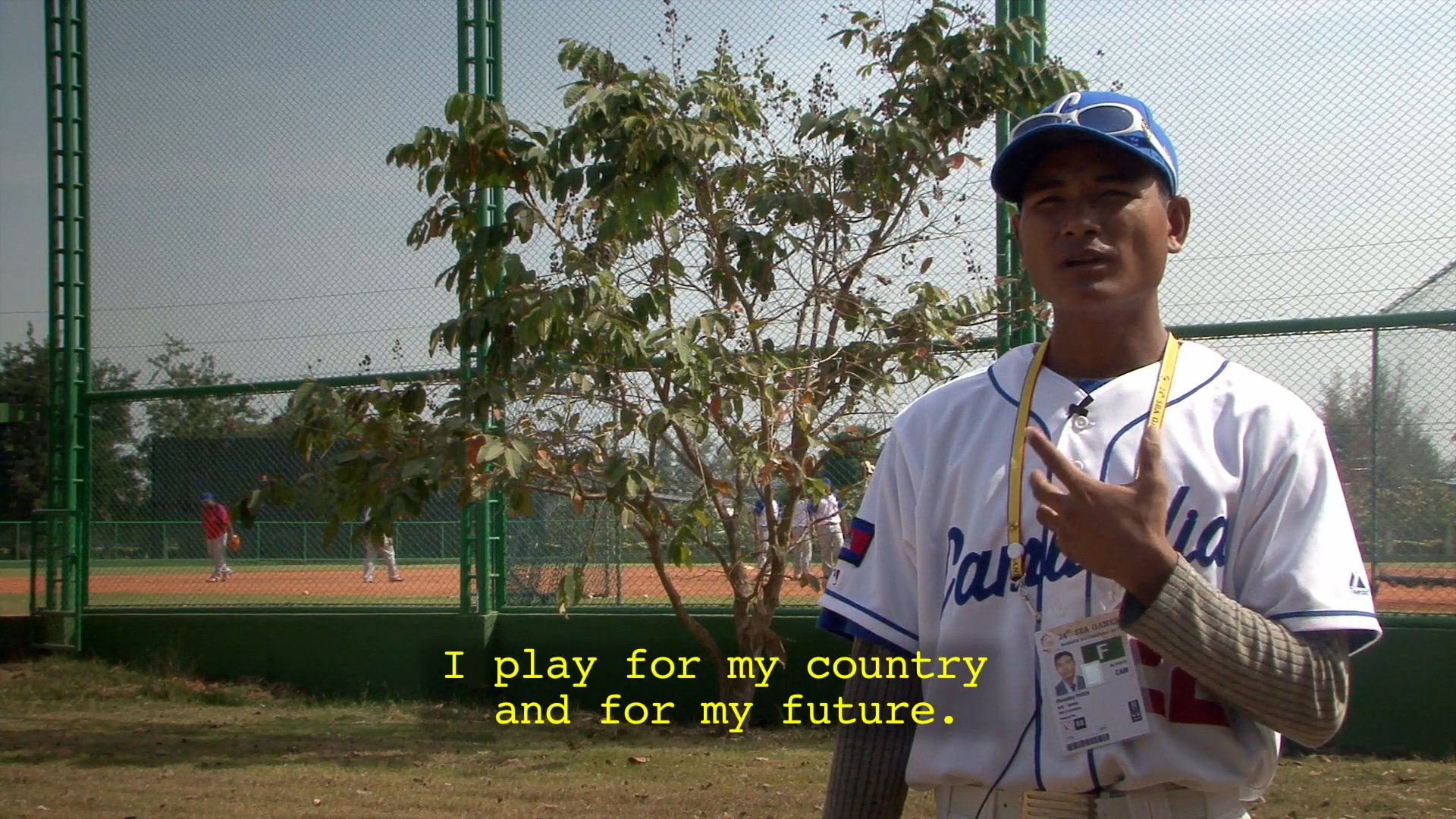 Members of the Cambodian national baseball team and coaching staff discuss their commitment to the sport and future aspirations while at a stadium.