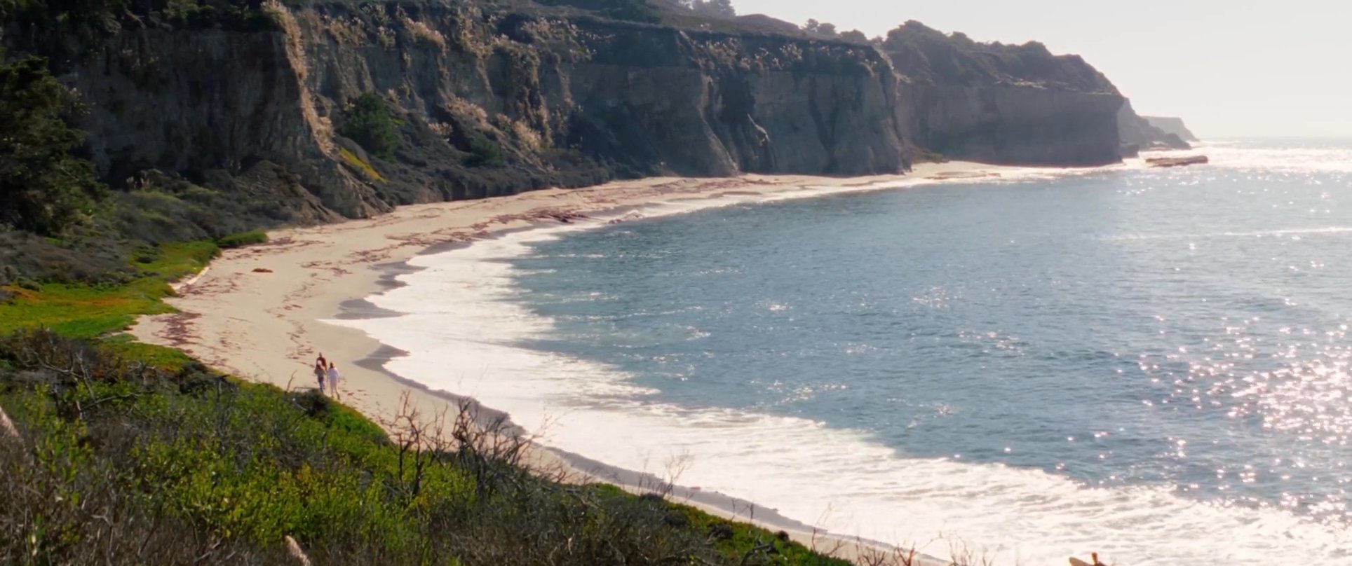 A group of people explores a rugged coastal landscape, transitioning from a scenic clifftop overlook to a walk along the shoreline.