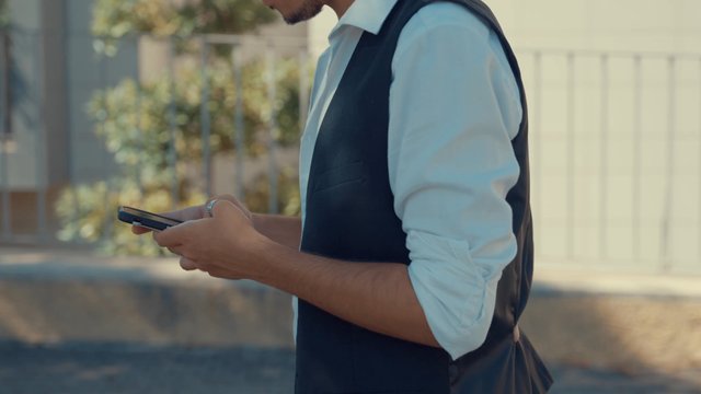A man using his smartphone while walking along a street 