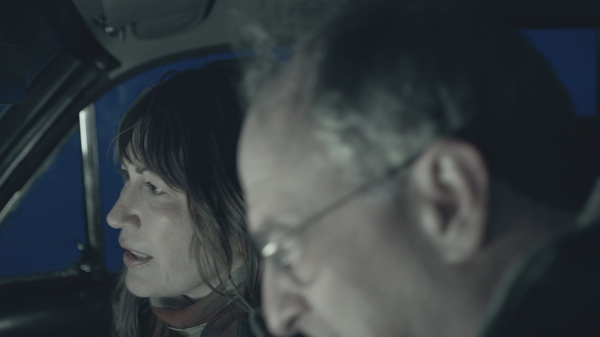 A man and a woman engage in a heated discussion inside a vehicle at night. The tension escalates as the driver turns the ignition key in an attempt to start the car.