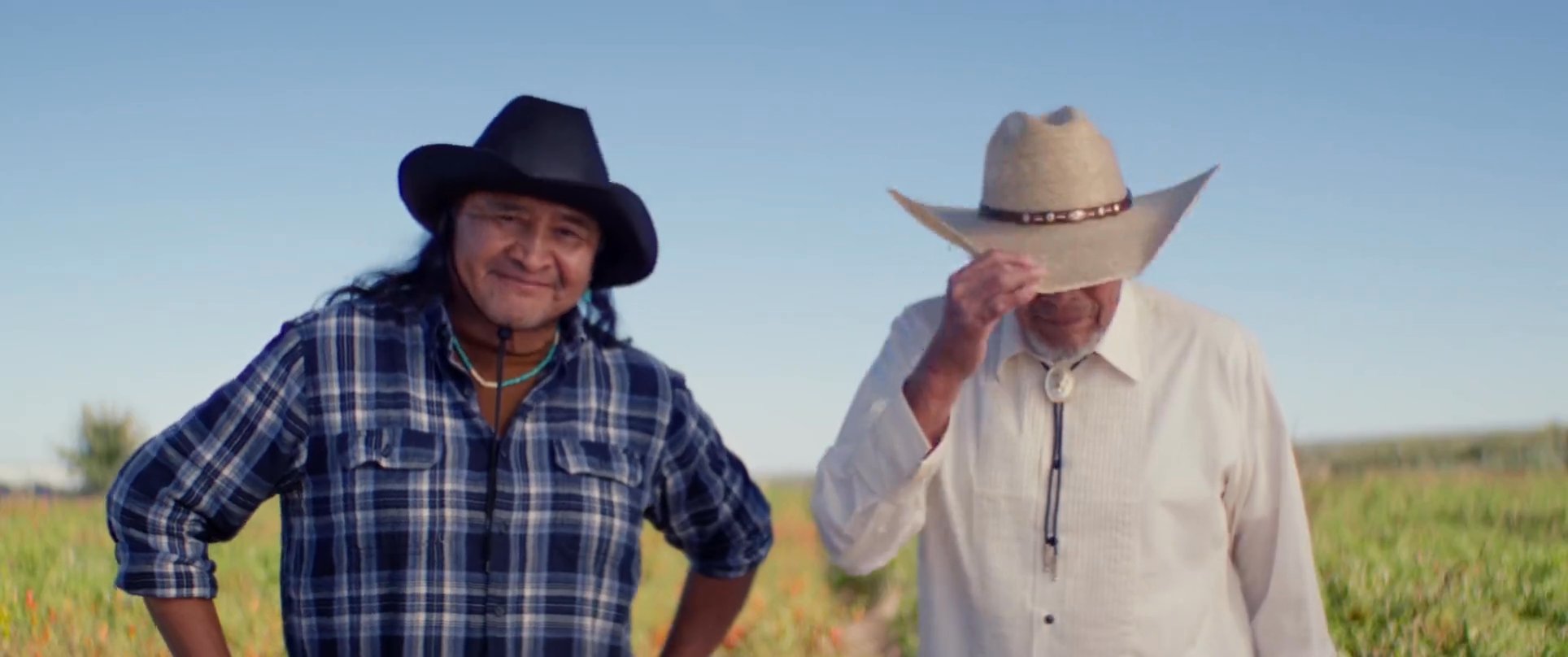 The sequence transitions between scenes of a surfer at dawn, intimate moments on a porch, and two men in cowboy hats sharing a lighthearted interaction in a field. The narrative concludes with expansive, serene shots of the ocean at sunset.