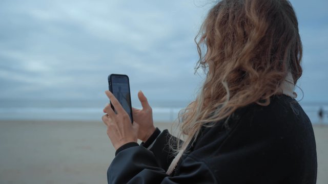 A girl recording a video on the beach with her smartphone
