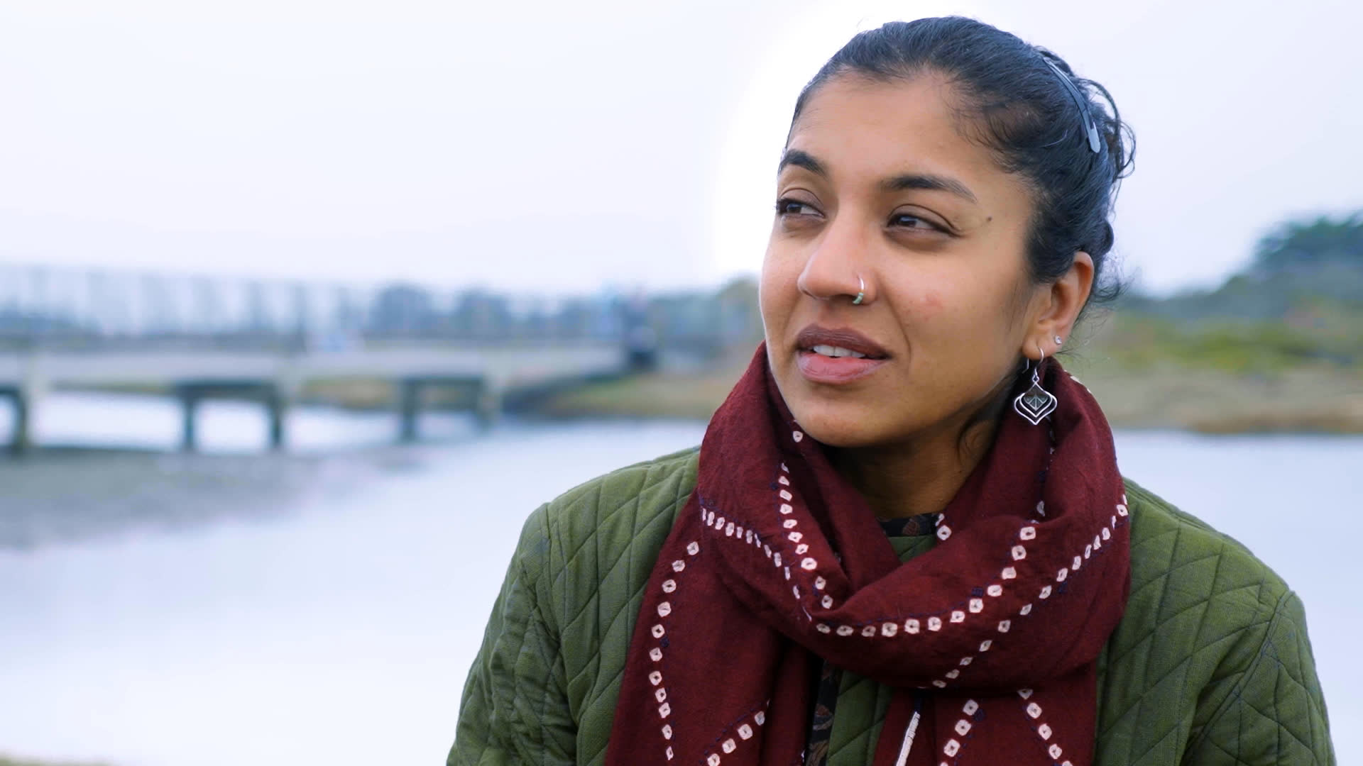 A woman discusses making the natural world accessible to diverse Bay Area communities, describing the park as 14 acres of magic. Nearby, people gather beneath a canopy and sit together outdoors by the waterfront.