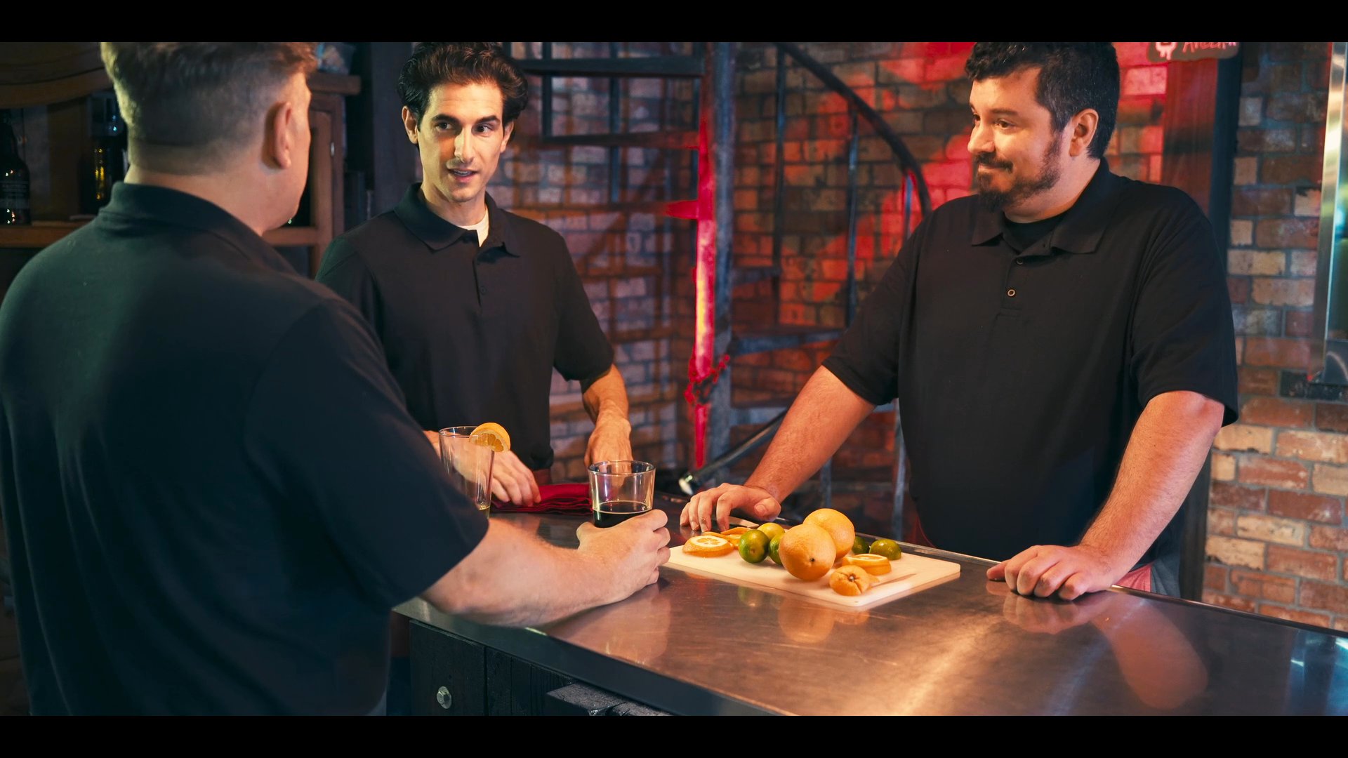 Three individuals converse in a modern brewery setting while evaluating craft beer samples paired with small appetizer snacks on the counter. The interaction reflects a professional tasting or hospitality demonstration in a rustic, industrial-style environment.