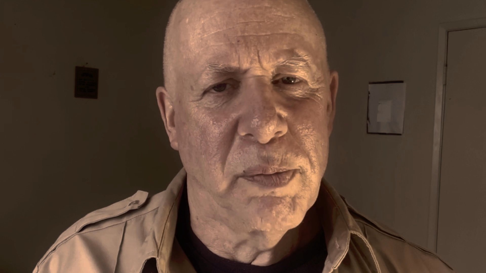A middle-aged man speaks directly to the camera in a serious and reflective tone. He occupies a dimly lit indoor space while maintaining steady eye contact.