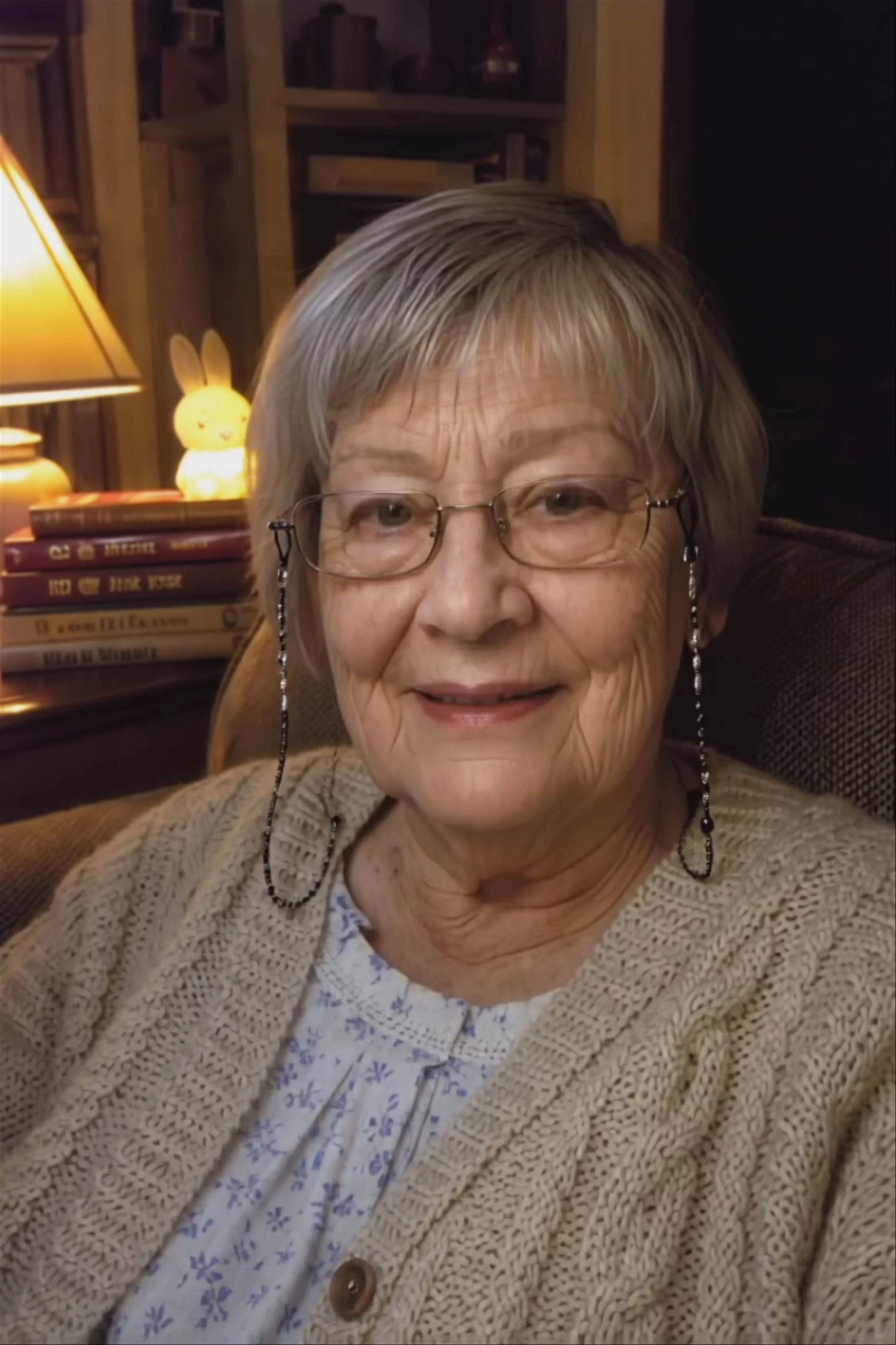 A vertical 720x1080 seated talking-head video of a warm elderly woman in a cozy armchair, telling a bedtime story to camera by lamplight. Generated from a still image and an audio track using Hedra Character 3.