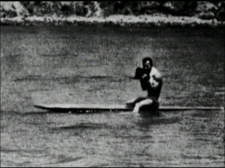 A filmmaker records surfing activity from the water before transitioning to shots of multiple surfers riding waves on their boards.