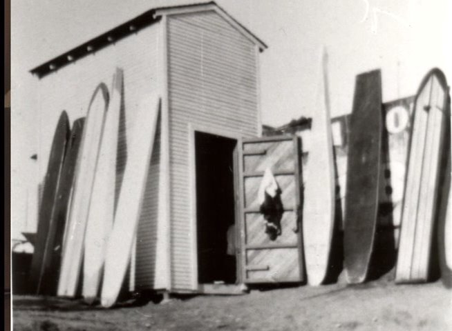 A man provides historical commentary as the presentation transitions into vintage black and white photographs of the Santa Cruz Surfing Club headquarters.