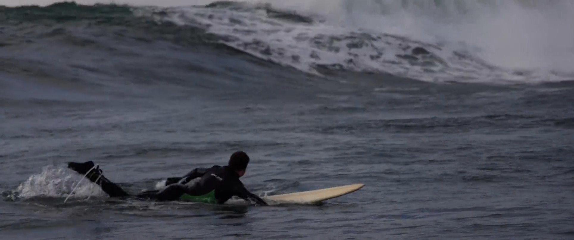 A surfer paddles across open water, positioning themselves to navigate and ride massive, breaking waves in the ocean.