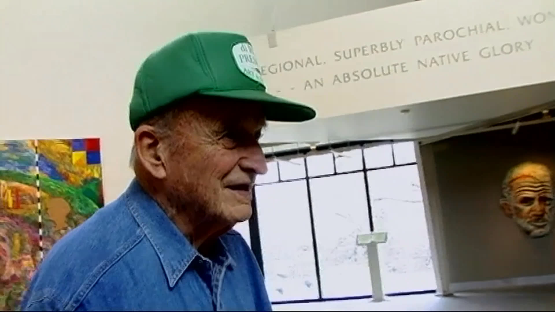 An elderly man in a green cap talks about memory loss after a stroke and the challenge of identifying artwork in a gallery without labels. Other visitors examine an ornate pink tiered sculpture in a glass display.
