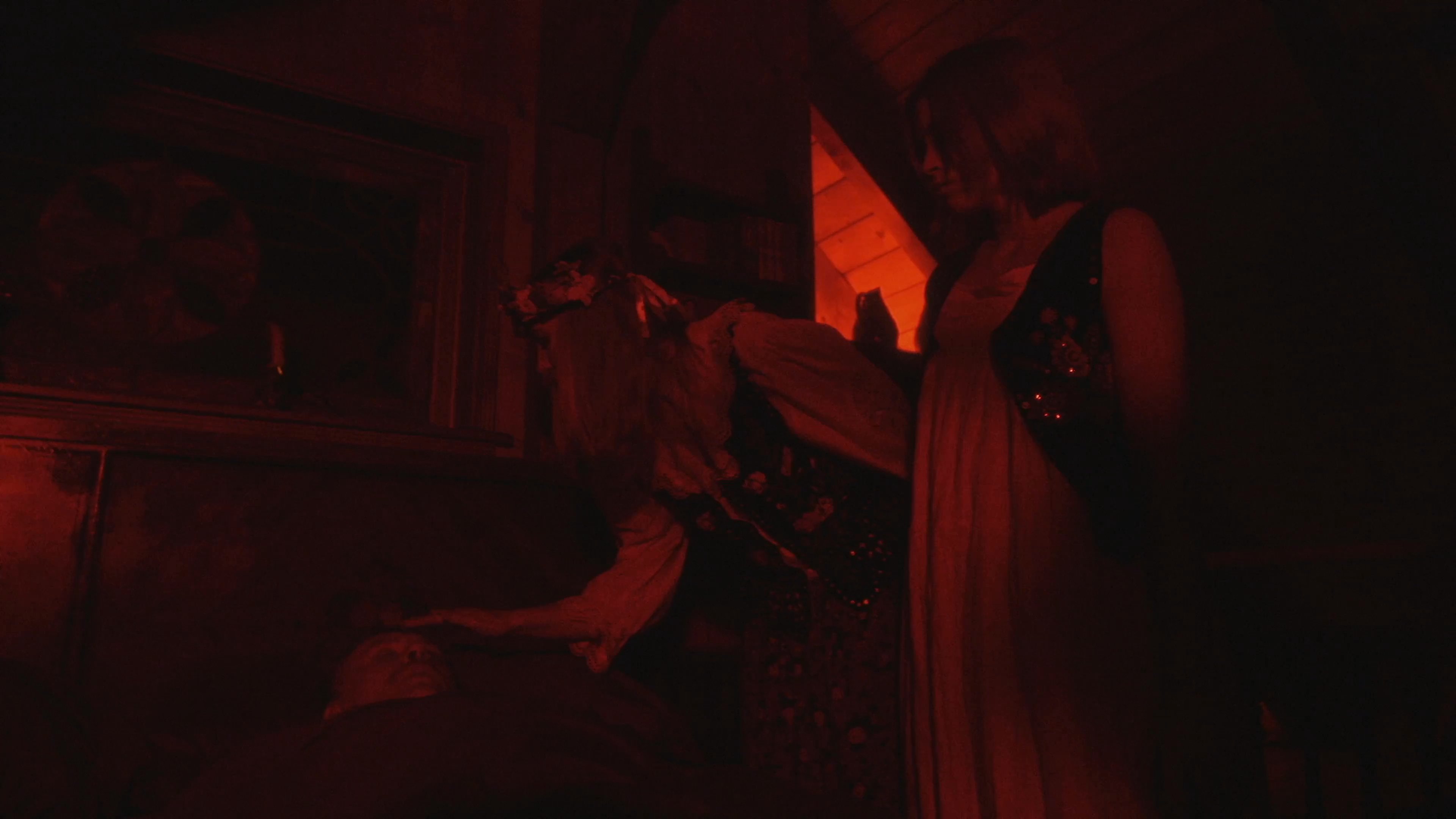 Two figures in traditional attire engage in a solemn exchange under dramatic red lighting, transitioning to a scene of intense emotional distress in a dimly lit, blue-toned interior.