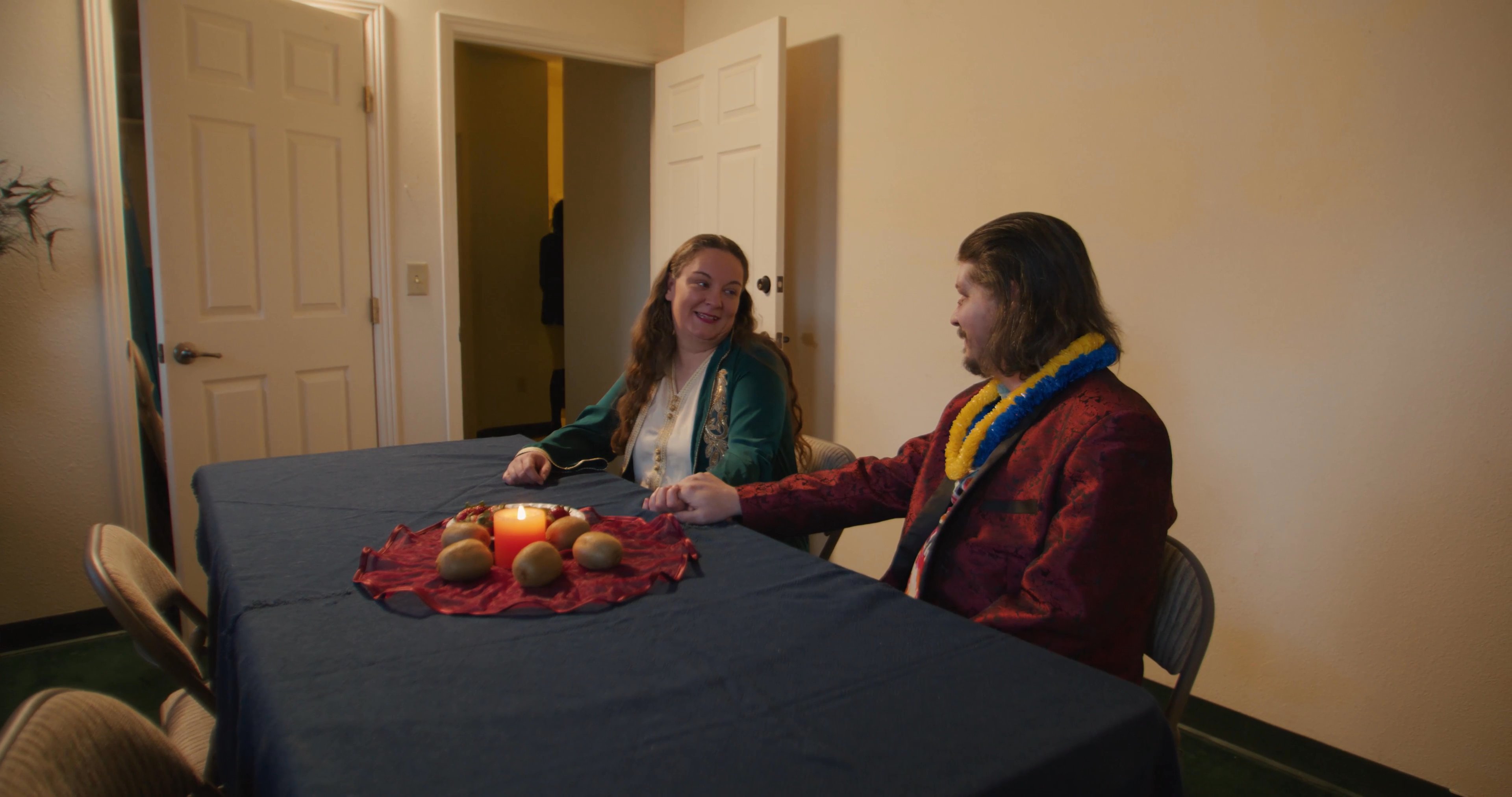 Participants engage in a conversation at a table before one individual prepares drinks using a container labeled formaldehyde in a nearby kitchen area.