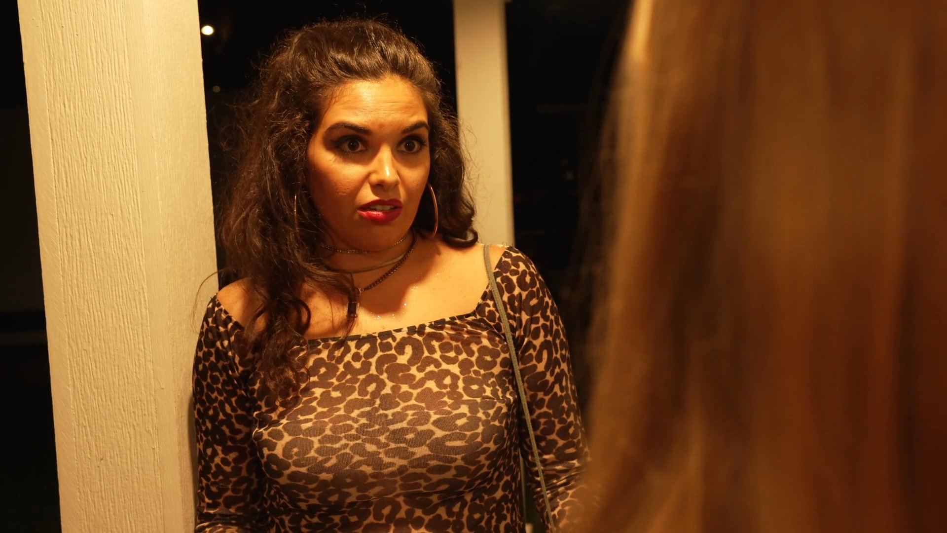 A woman participates in an off-screen conversation, displaying a range of emotive facial expressions and communicative gestures in a dimly lit setting.