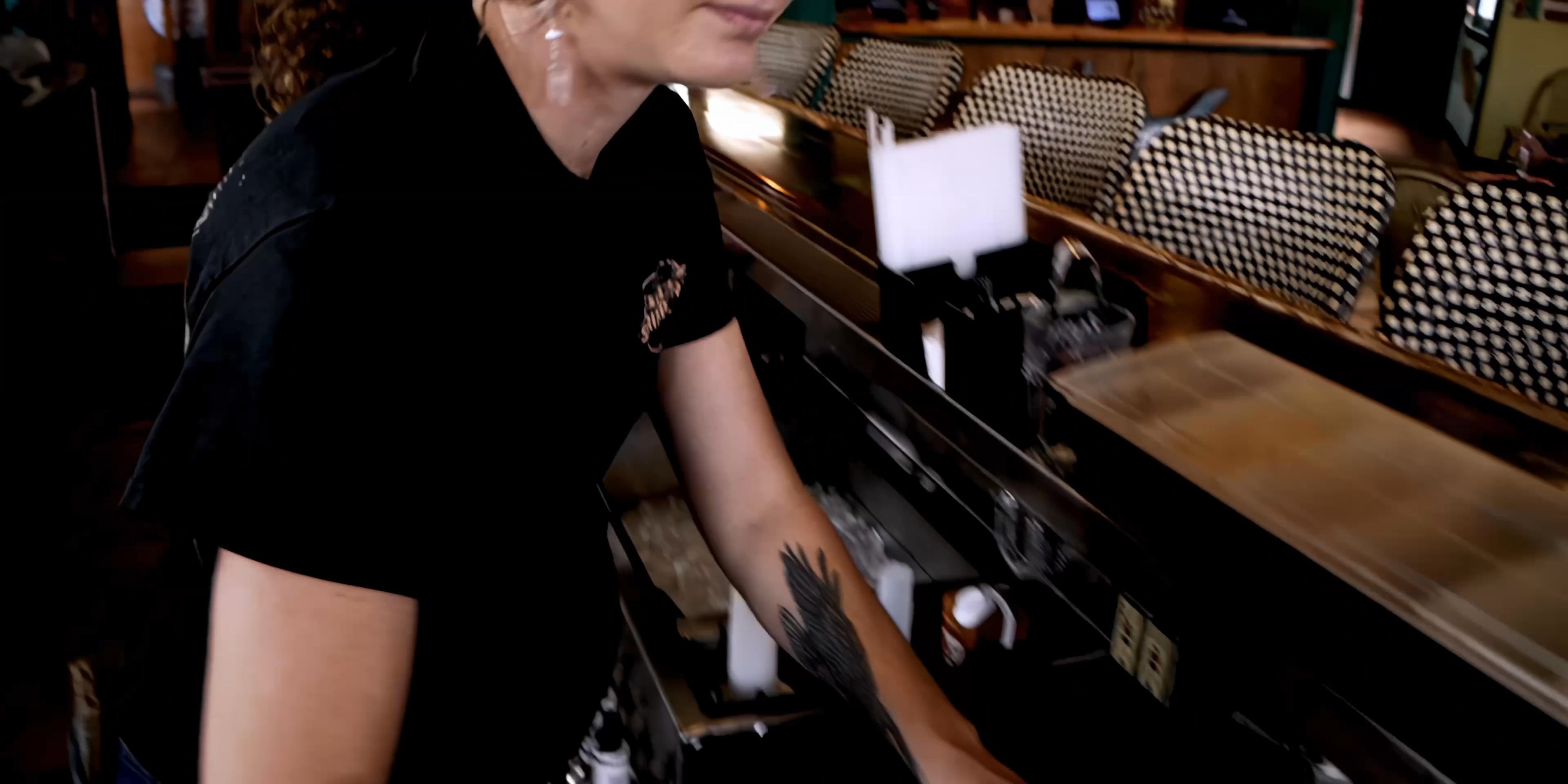 A bartender expertly prepares beverages behind a restaurant bar while patrons socialize in the background during an evening shift.