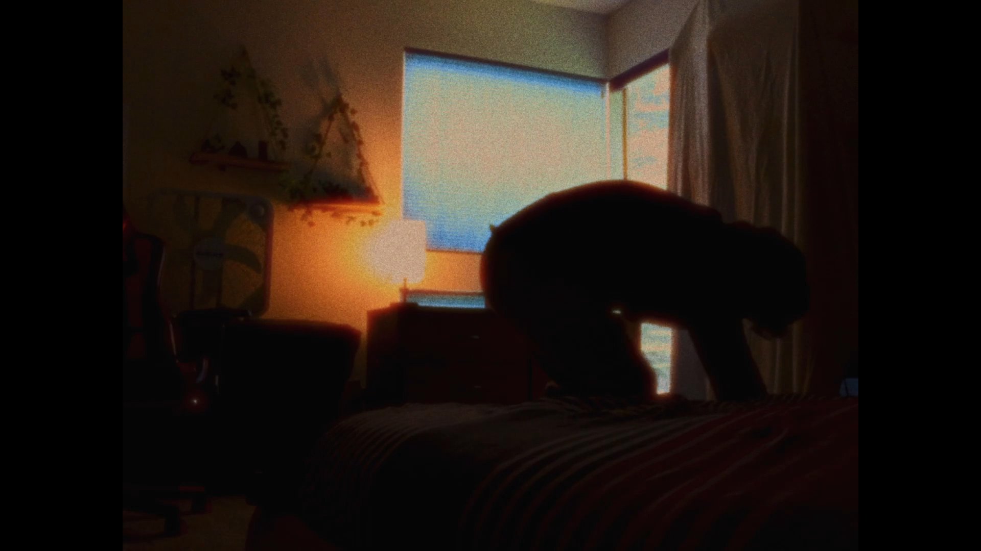A person wakes up in a dimly lit bedroom and rises from the bed to approach a window in the morning light. The scene captures a quiet, contemplative start to the day.