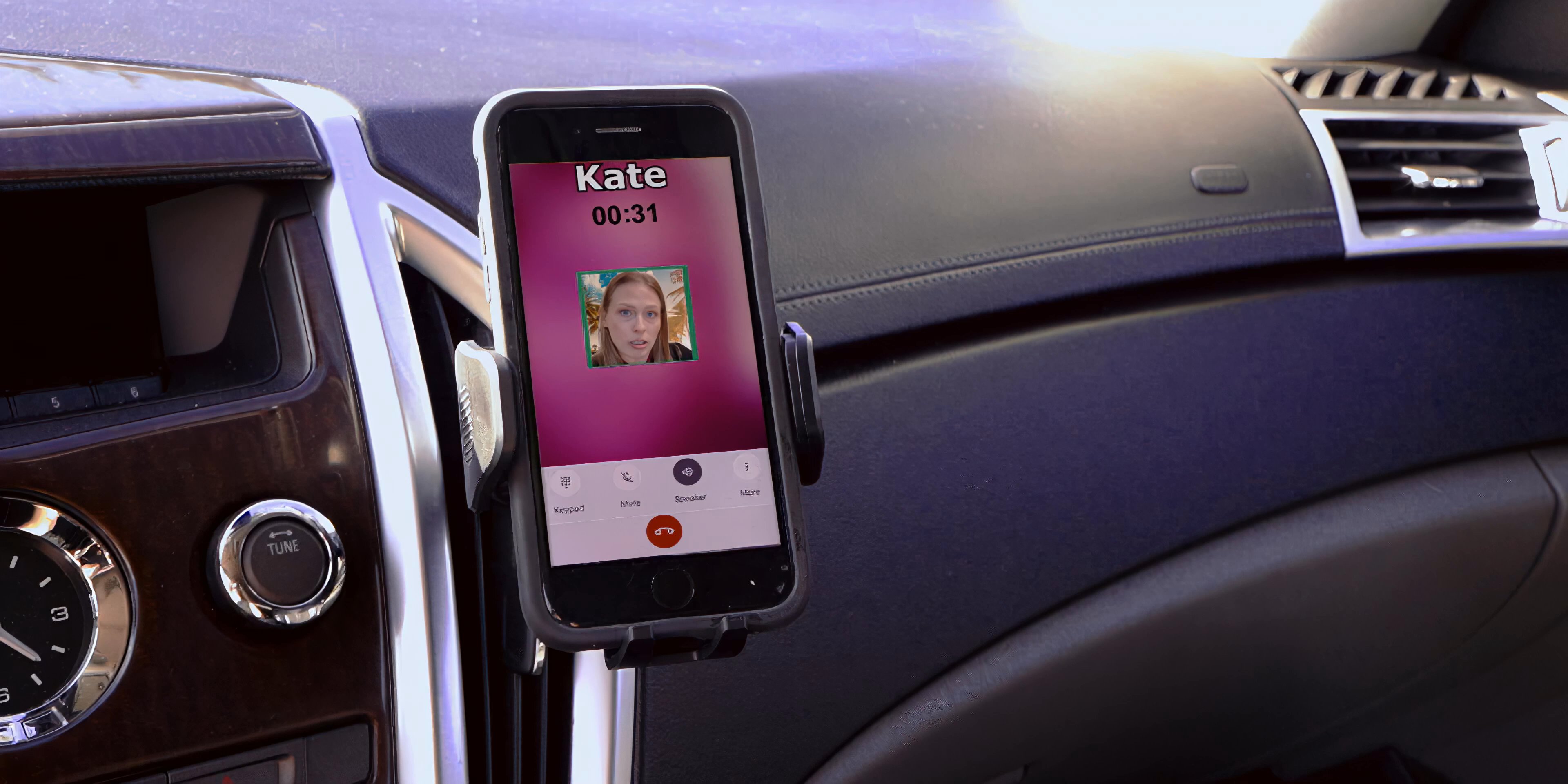 A man sits in the driver seat of a parked car while receiving an incoming phone call from Kate. He observes the urban surroundings while the call screen remains active on the dashboard mount.
