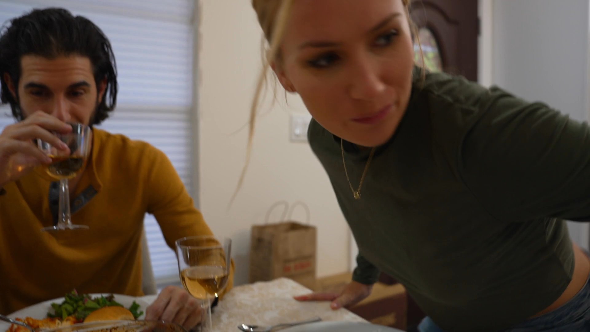 Friends gather for a celebratory holiday meal in a home setting, featuring a roasted turkey and shared conversation. Guests arrive and socialize while enjoying a formal dinner together.