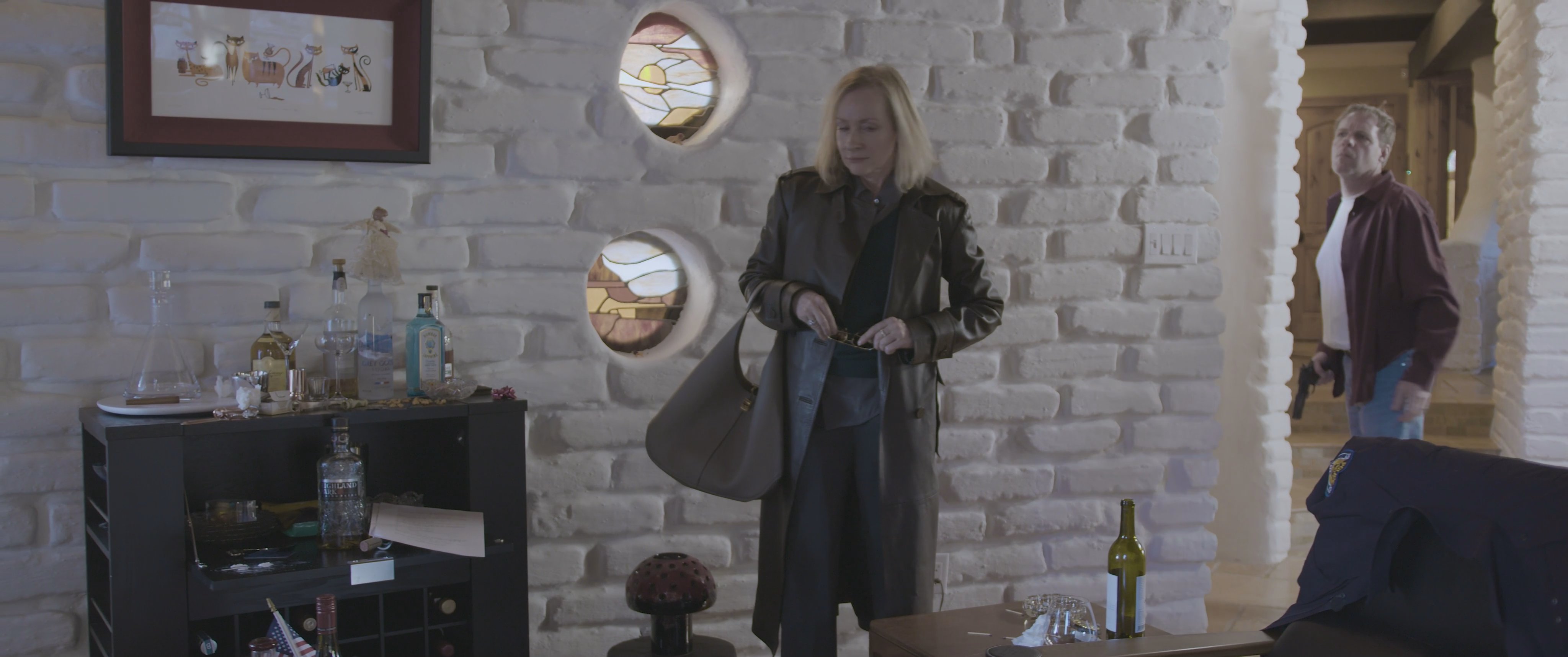 A man and a woman engage in a quiet, serious conversation inside a living room before the woman prepares to depart. The scene captures a moment of interpersonal tension and transition within a residential setting.