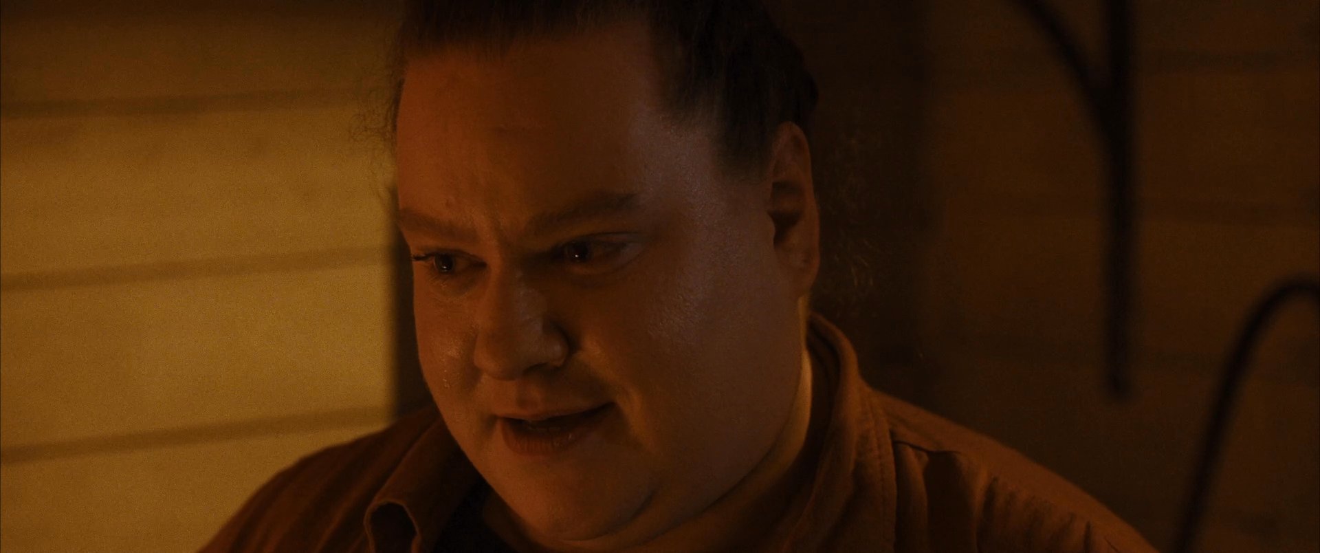 A man speaks with focused intensity while illuminated in a dimly lit, warm-toned environment. His facial expressions shift as he communicates his message during this intimate, close-up interaction.