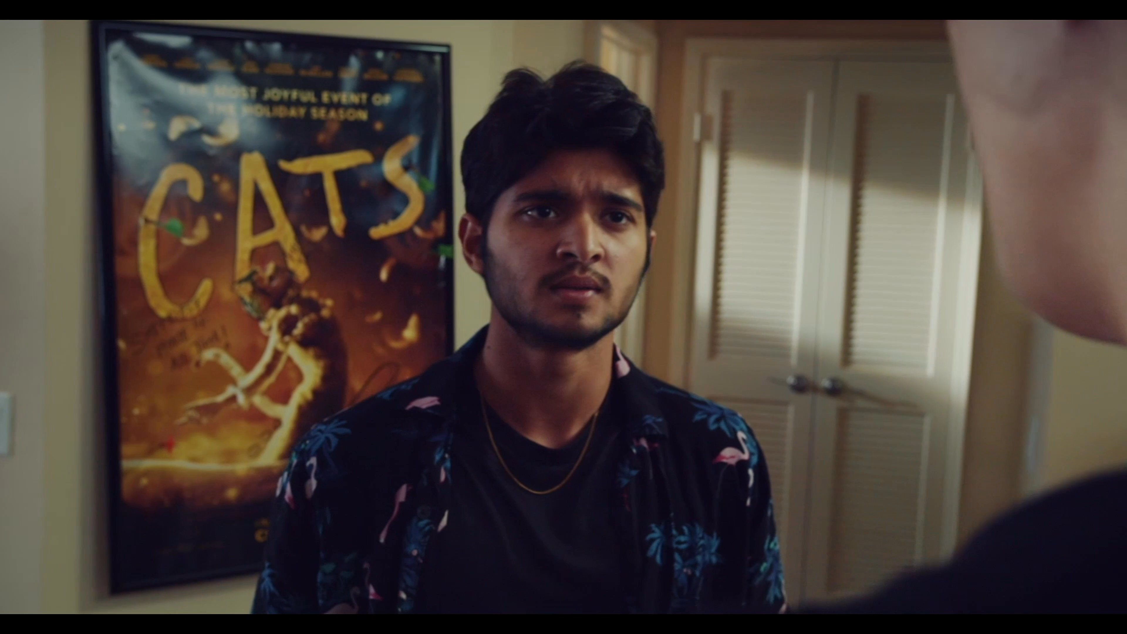 Three young men engage in a tense conversation inside a residential living space. The interaction involves expressive gestures and focused dialogue as the individuals address a specific conflict or situation.