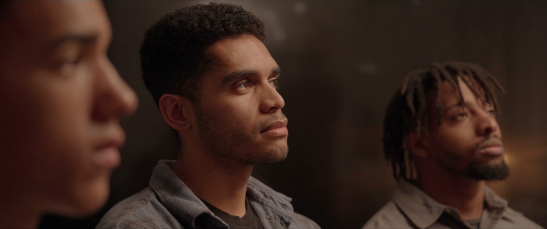 A man addresses the camera in a professional setting, interspersed with shots of a group of listeners observing the conversation.