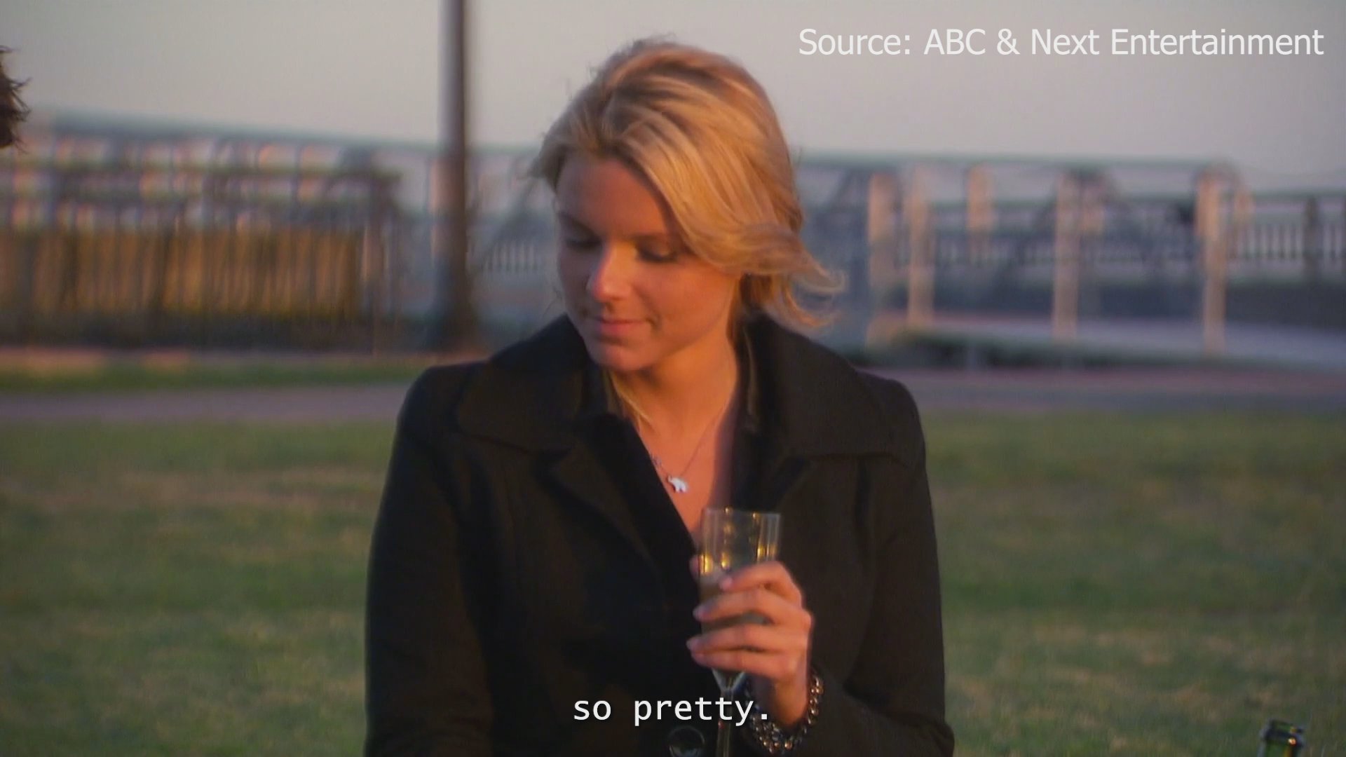 A man and woman engage in a heartfelt conversation outdoors, with a helicopter parked in the background at sunset.