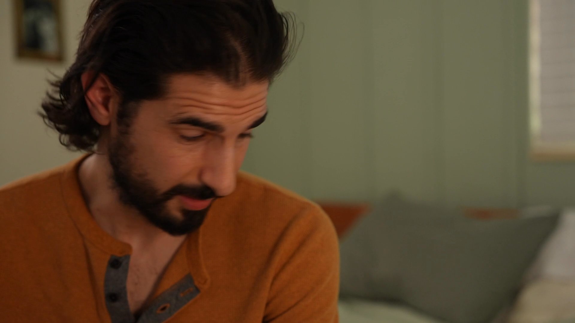 A man in a bedroom observes a sleeping woman before shifting focus, conveying a somber and reflective mood within a domestic setting.