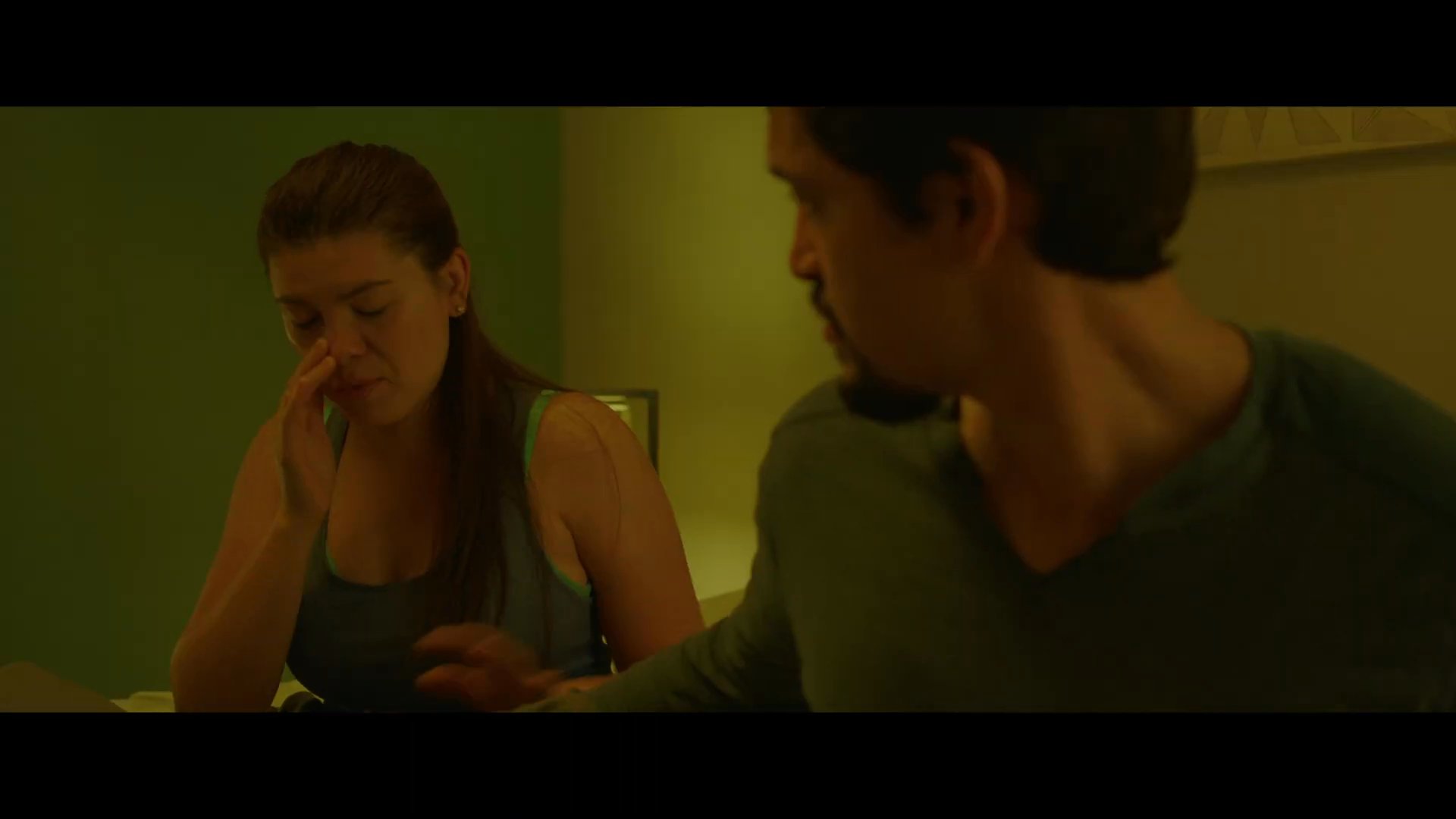 A man and woman discuss a serious matter in their bedroom at night while their young daughter is present. The dialogue exchange between the couple reflects visible emotional weight and interpersonal tension.