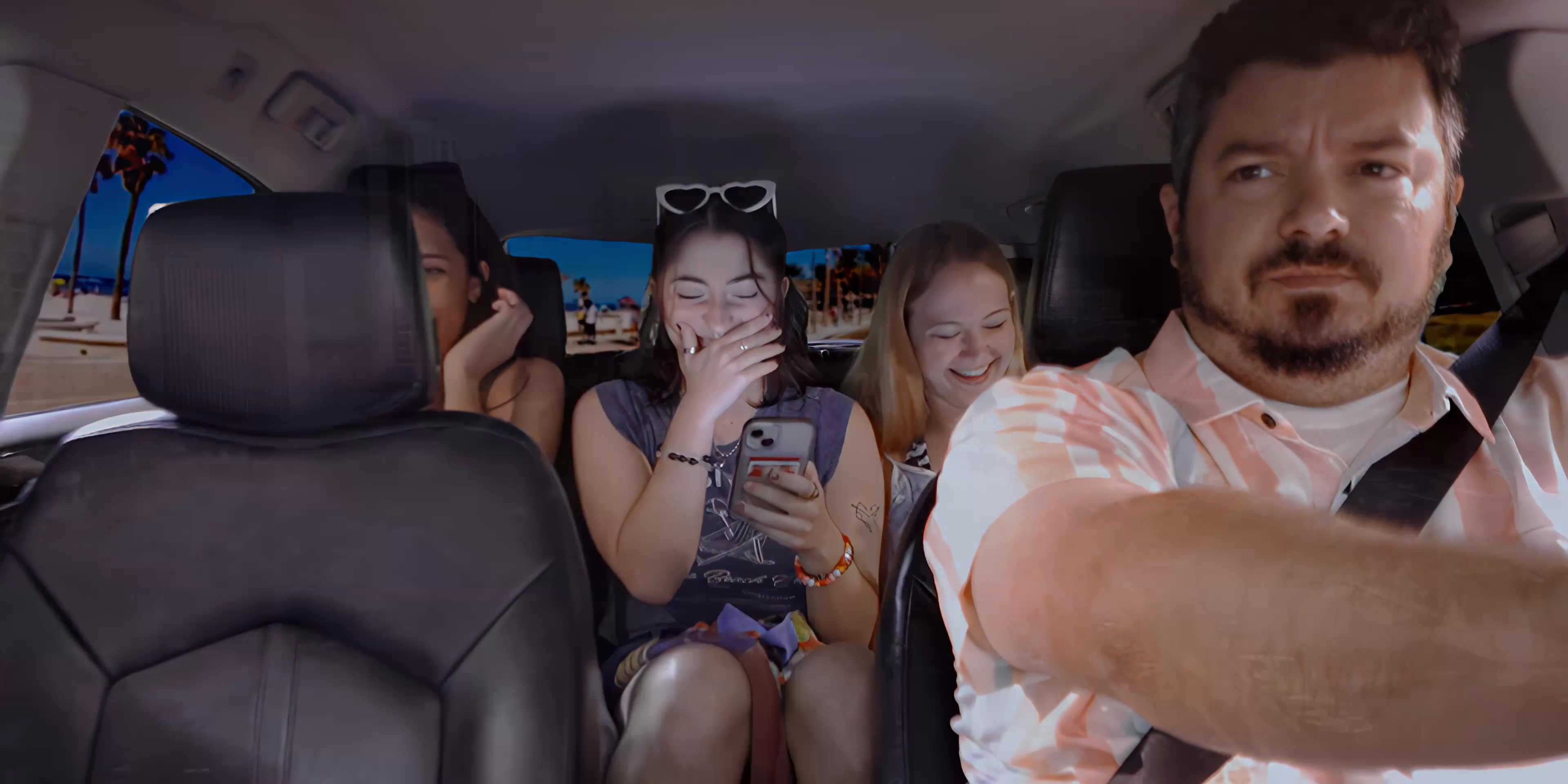 A man drives his family through a coastal city, shifting from an interior view of passengers to exterior drone shots of the urban waterfront and palm-lined streets.