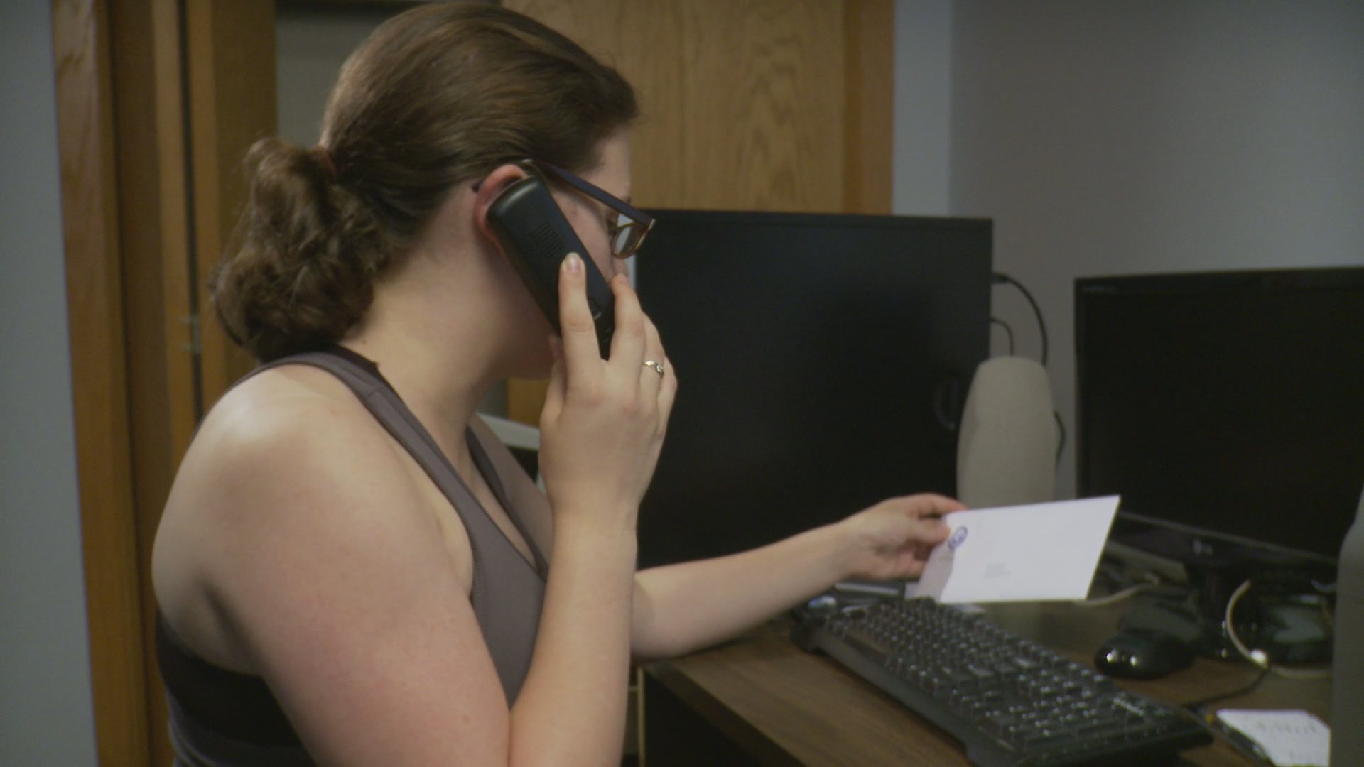 A woman and an older man participate in separate phone conversations while working in their respective home environments. Both individuals appear focused on managing tasks while engaged in professional or personal remote communication.