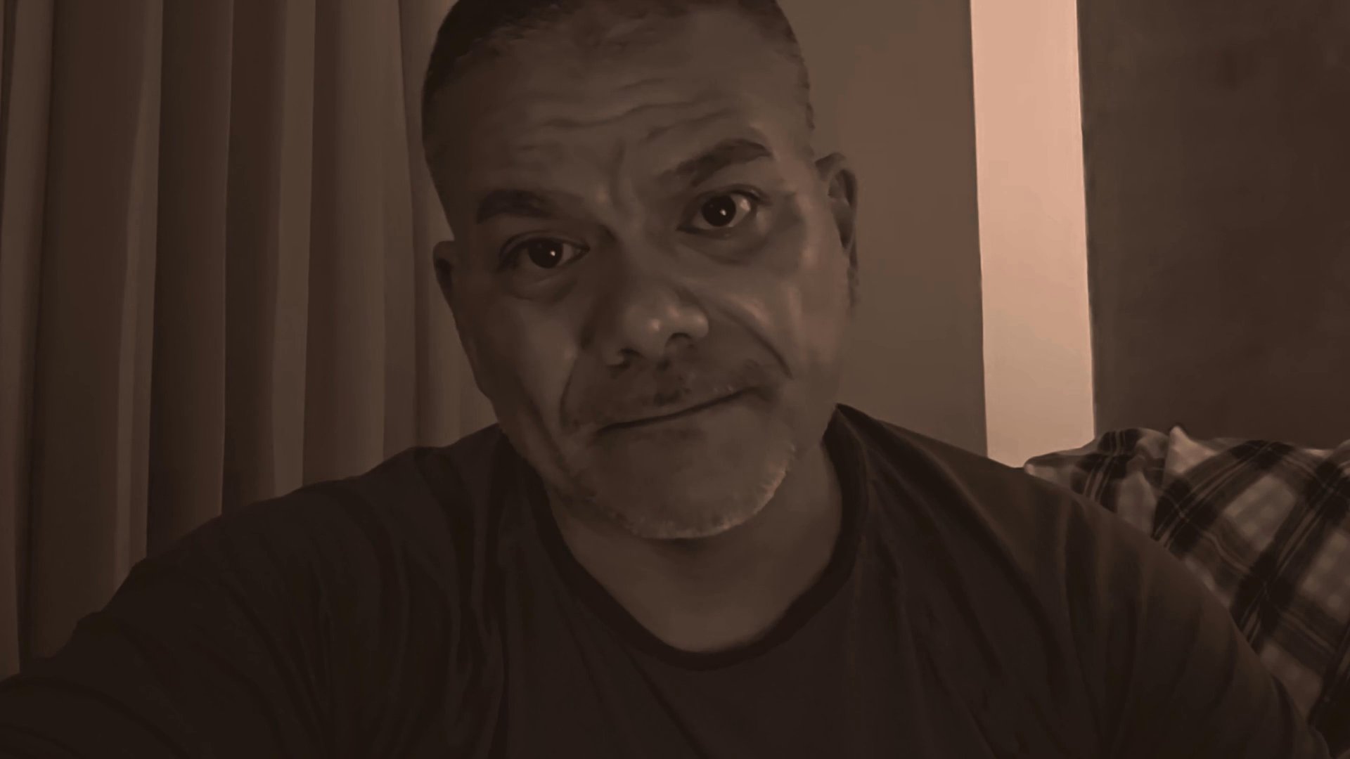 A man speaks directly to the camera, sharing thoughts in a conversational, informal indoor setting.