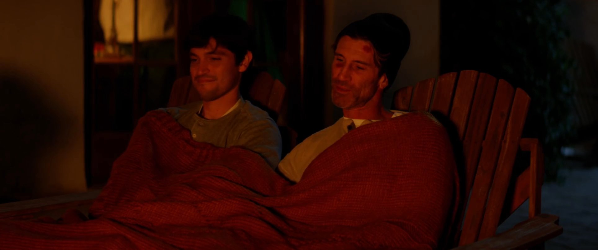 Two individuals engage in a quiet, intimate conversation while sitting together by a fire pit at night. The scene transitions between close-up portraits and the warm, ambient glow of the fire against the dark sky.