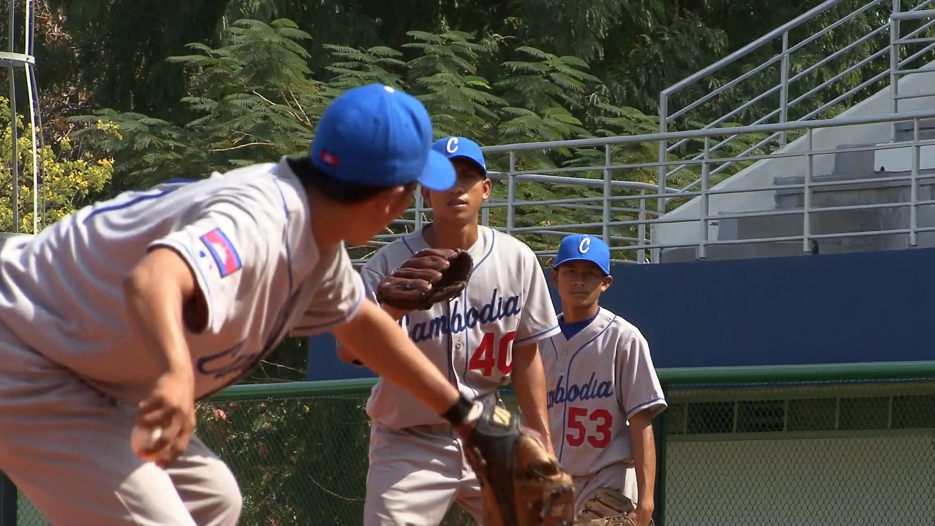 Athletes perform baseball pitching and fielding drills on a dirt diamond during an organized team practice session.