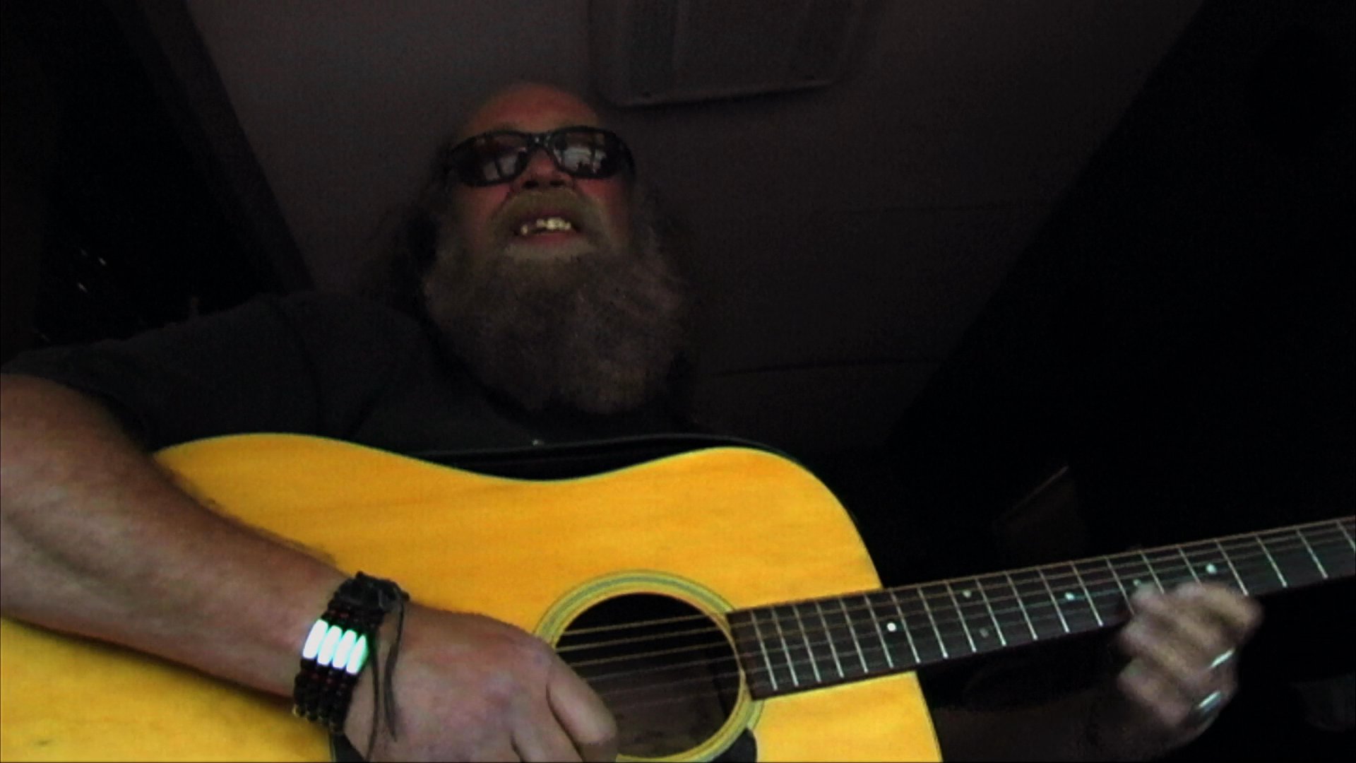 A bearded man plays an acoustic guitar while riding in a vehicle, transitioning to footage of a man driving and concluding with a close-up of Willie Nelson.