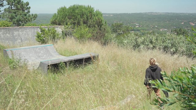 A guy walking to a half-pipe skating ramp in a field