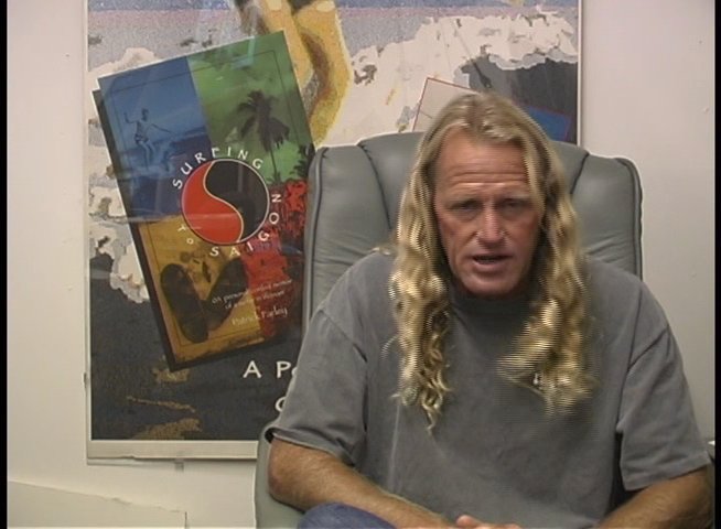 A long-haired surfer sits in an office chair and gestures while sharing his professional experiences and insights during an interview.