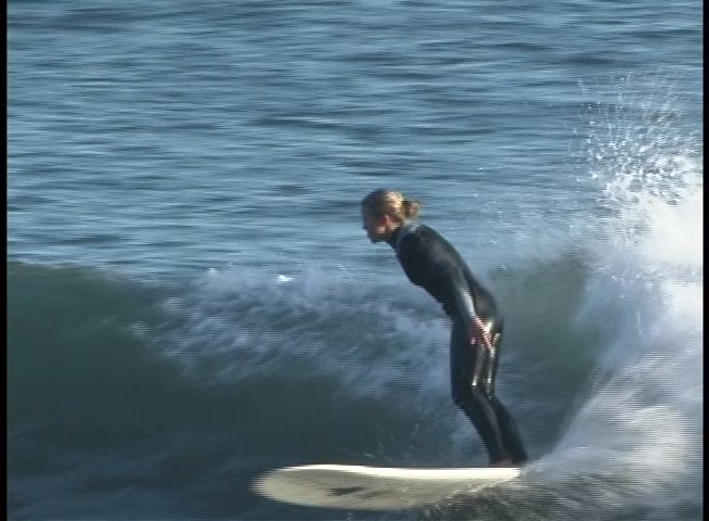 A surfer in a black wetsuit skillfully navigates rolling ocean waves before transitioning to a perspective of a man observing the activity. The sequence highlights athletic movement on the water followed by a brief instructional or interview segment.