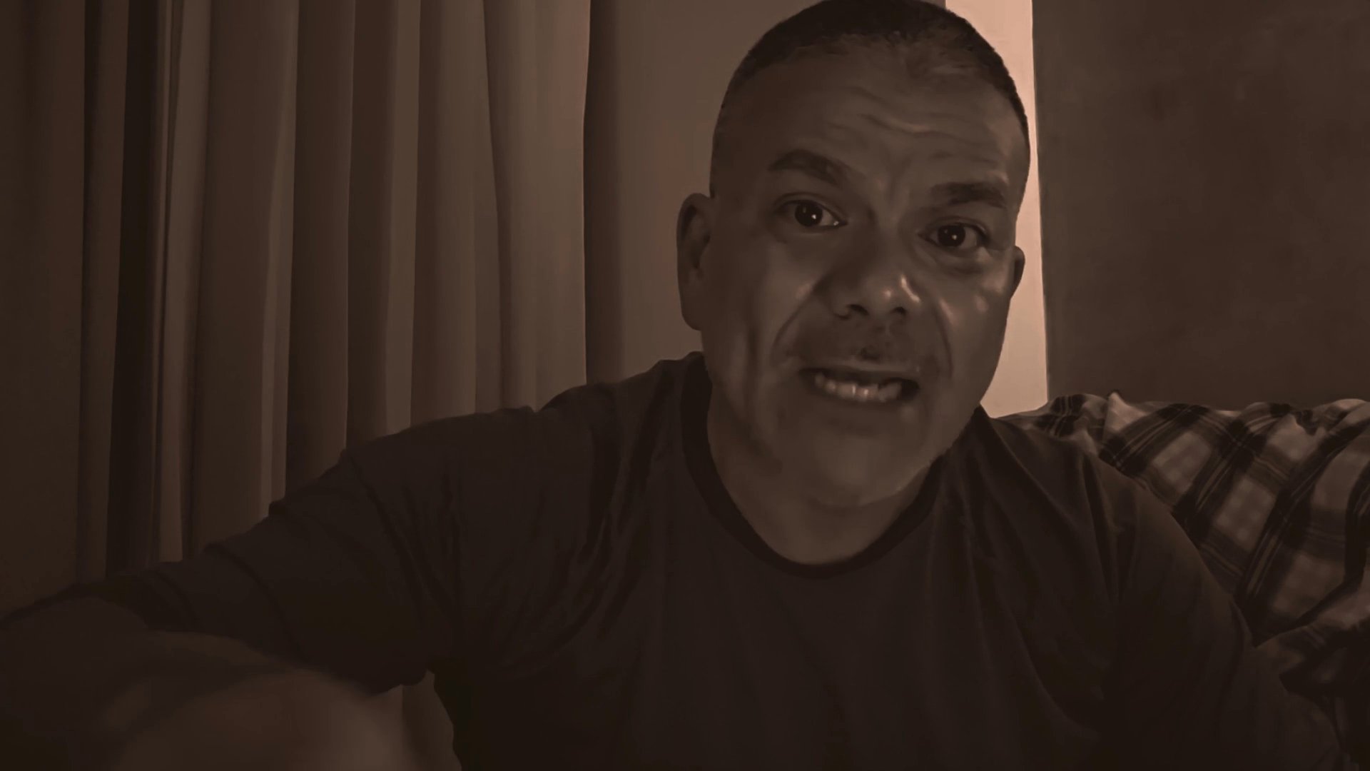 A man addresses the viewer directly, articulating thoughts with purposeful hand gestures in an indoor setting.