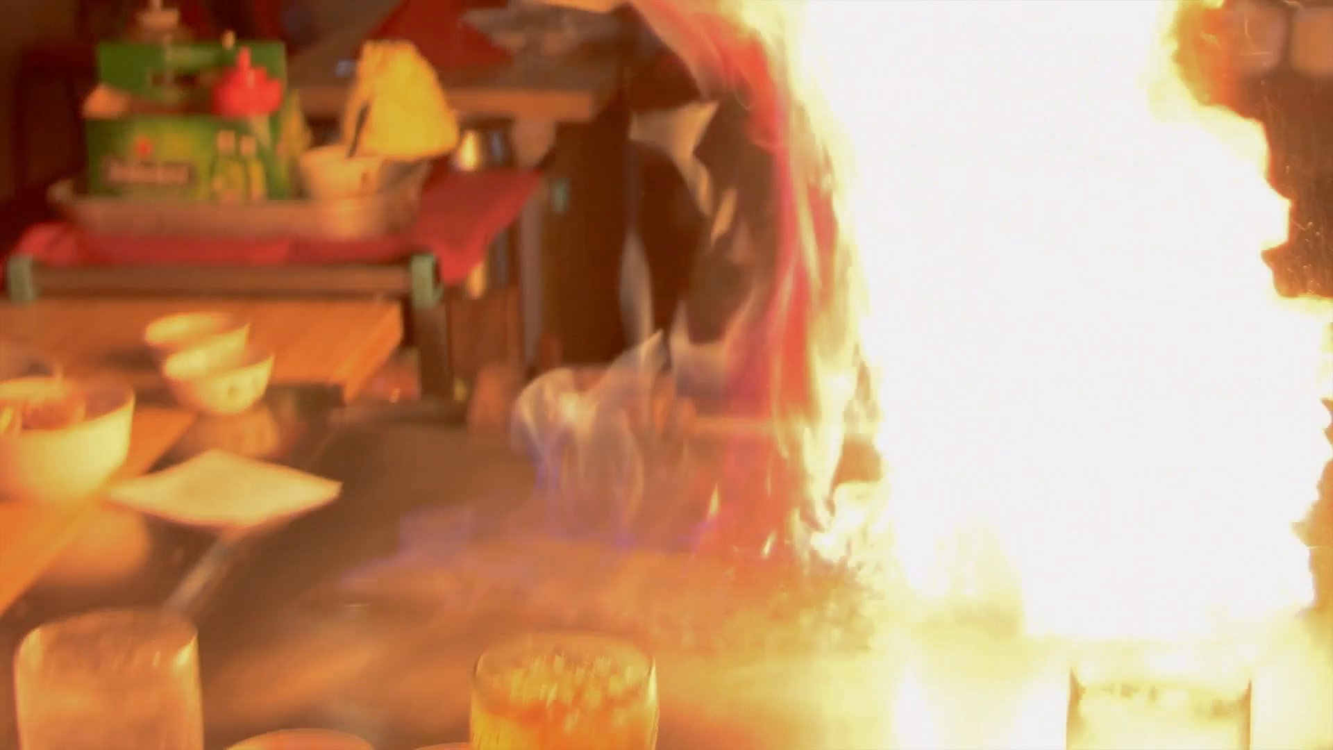 A chef performs a hibachi cooking demonstration for guests in a restaurant setting. The scene transitions to exterior footage of a street in Baribo, Cambodia.