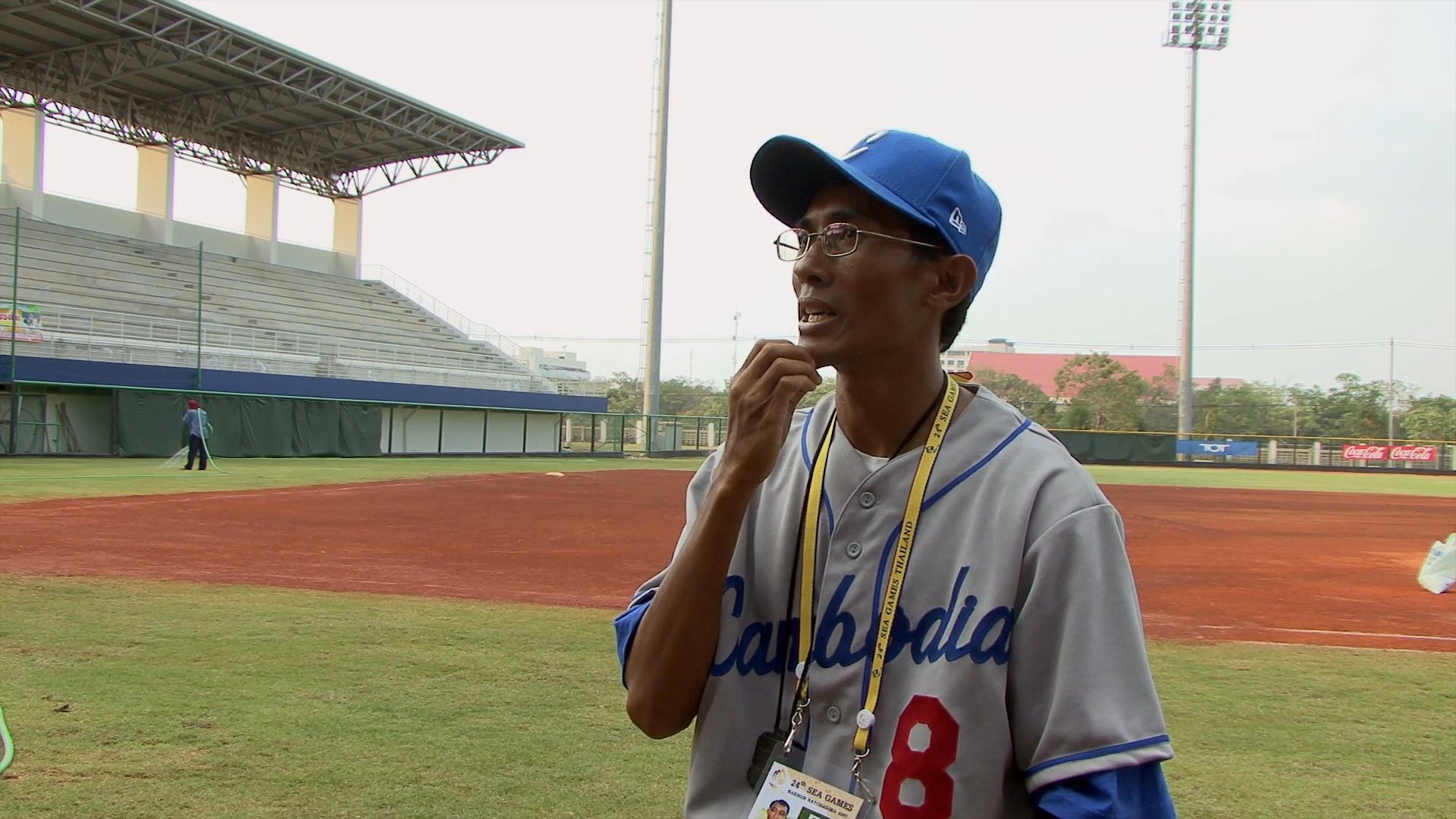 A baseball player in uniform stands on a stadium field, gesturing while discussing his experience during an interview.