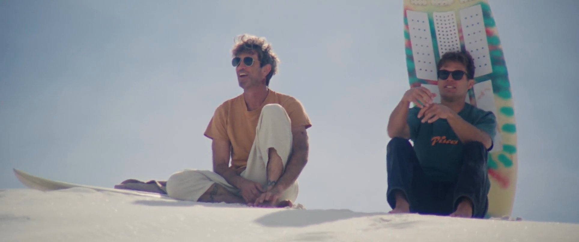 Two individuals practice sandboarding on expansive white dunes before walking together into the sunset. The sequence highlights a shared recreational experience in a desert landscape.