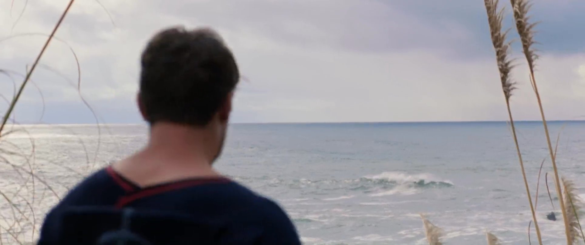 A surfer steps out of a vintage truck and prepares to enter the ocean along a rugged coastline. He observes the crashing waves before walking across the sand towards the water with his surfboard.