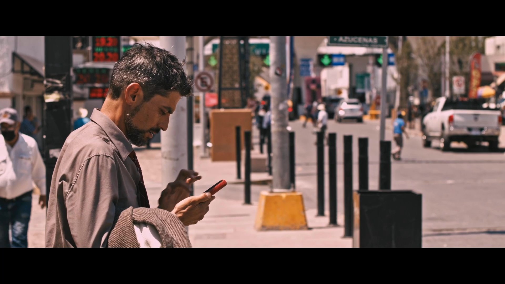 Two individuals engage in a brief conversation on a city street before one proceeds to place a phone call. The scene unfolds in an outdoor urban setting during daylight.
