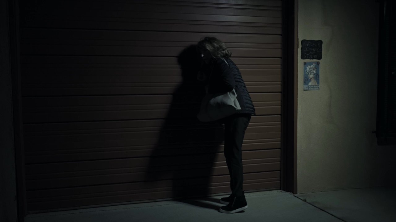 A woman arrives at the Marcella Ibanez Art Studio at night and is greeted by a male artist inside the workspace.