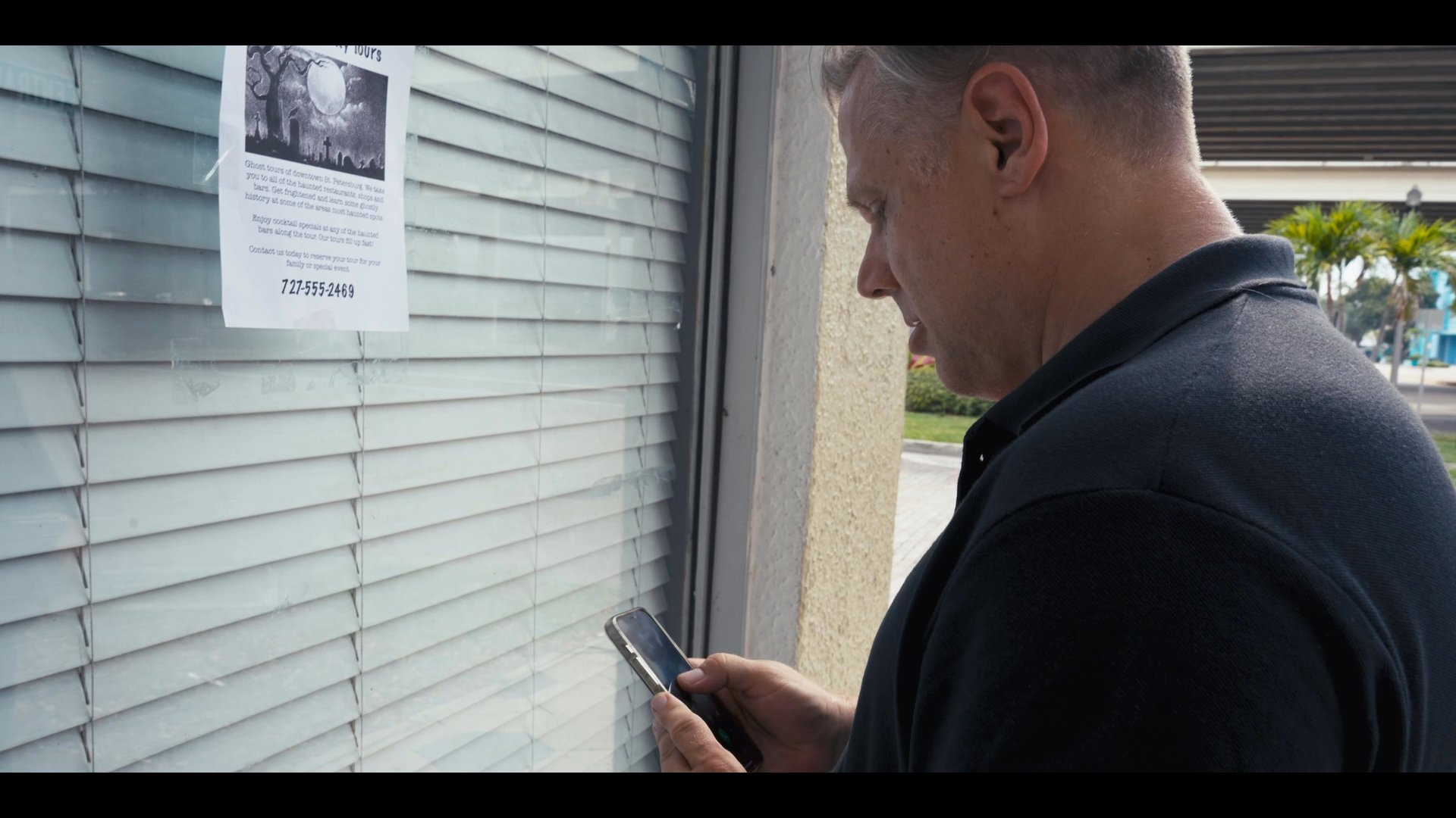 A man captures a photo of a flyer for local ghost tours before making a phone call to inquire about the service.