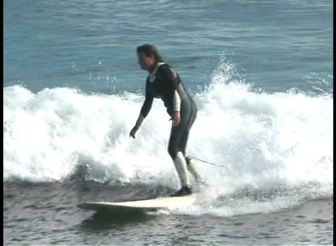 A skilled individual in a wetsuit maneuvers a surfboard across rolling ocean waves. The session demonstrates balance and technique while navigating the water surface.