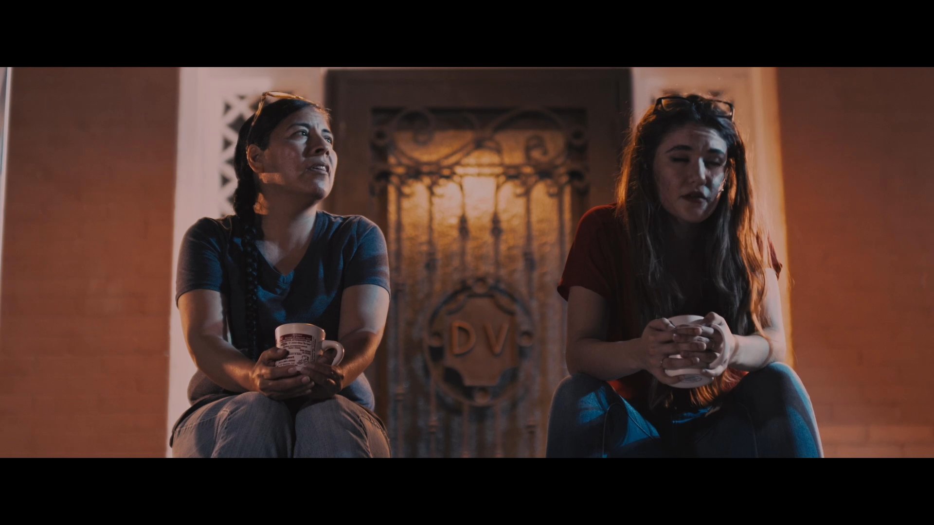 Two women sit together on a balcony at night, engaging in a quiet and personal conversation while holding mugs. The dialogue transitions into a discussion about a past relationship.