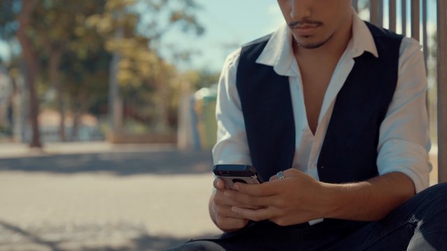 A man typing on his phone while sitting on the curb