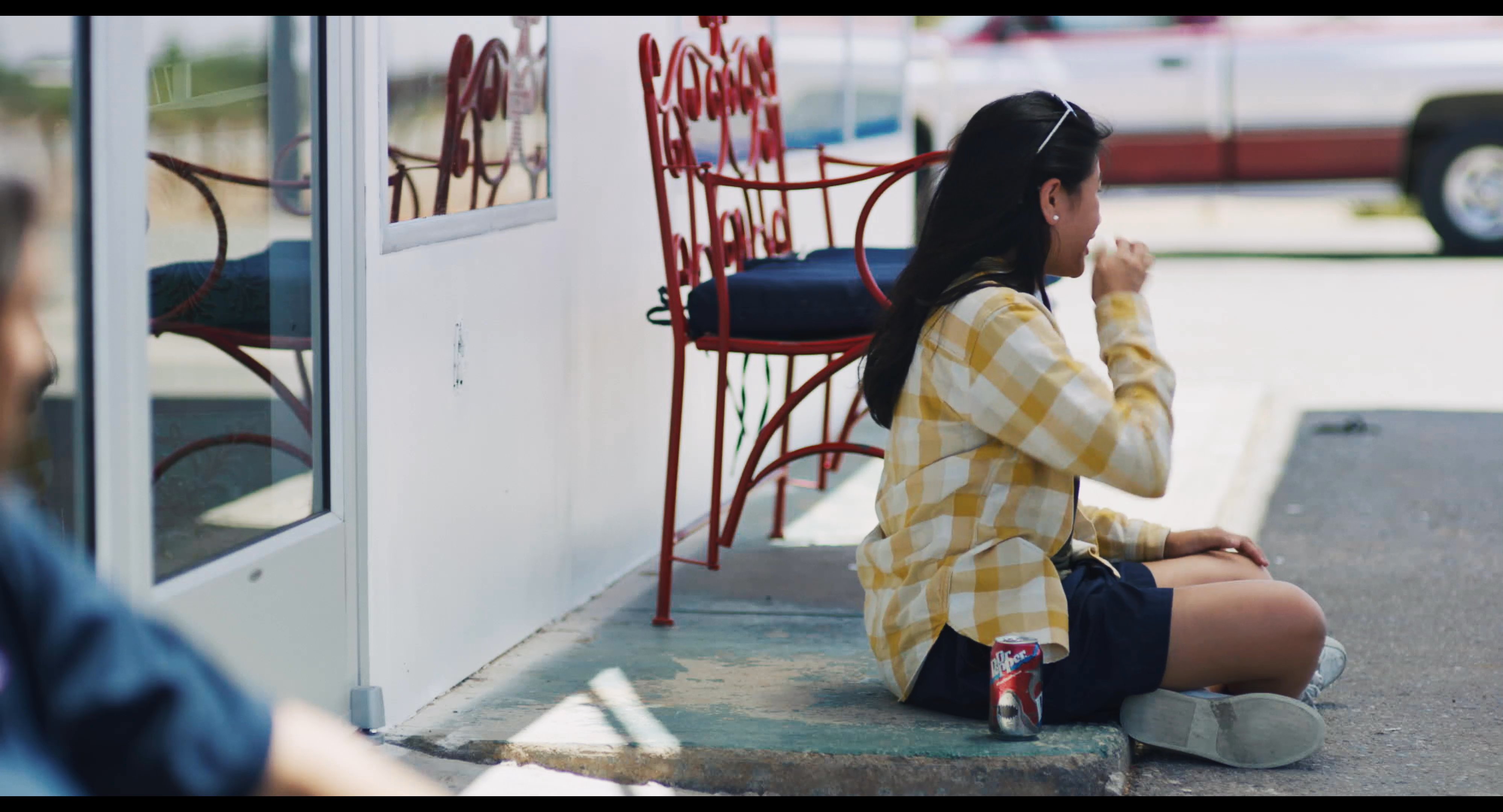 A man and a woman engage in a quiet conversation while sitting on the pavement outside a building. They exchange words in a relaxed, reflective setting.