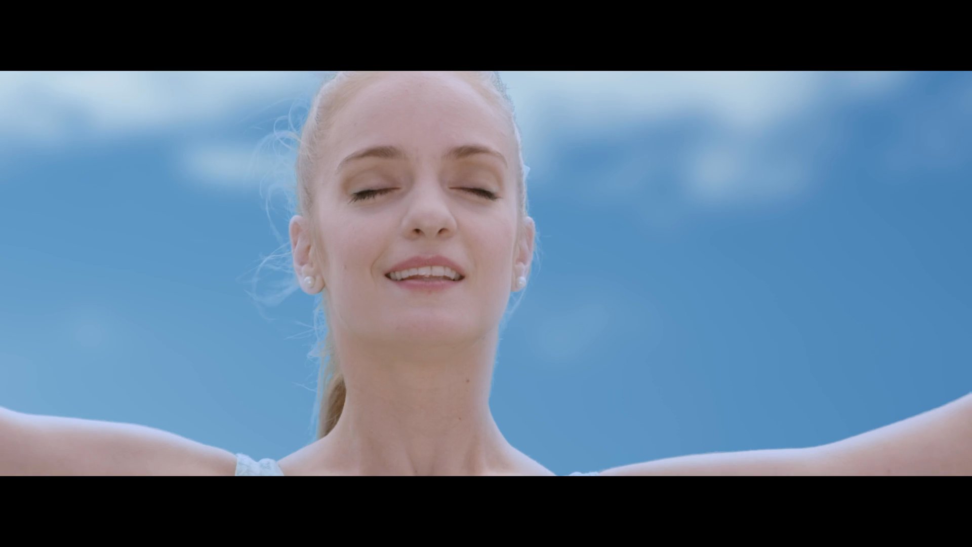 A ballet dancer performs a routine in a bustling outdoor plaza accompanied by a cellist while spectators watch. The scene transitions to the dancer interacting with a partner as an audience observes the artistic display.